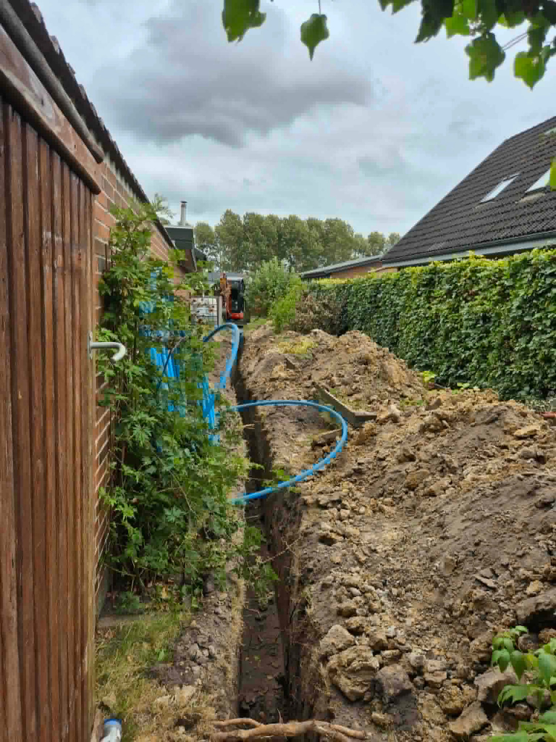 Blå vandledning lagt i smal rende i baghave med minigraver i baggrunden